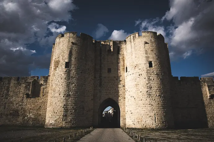 aigues mortes a large stone castle with a walkway leading to it
